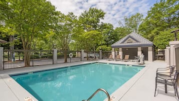 Piscina rectangular con una escalera metálica, rodeada por una cerca y árboles.
