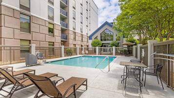 A swimming pool with lounge chairs and tables, surrounded by a building with balconies and a covered patio area.