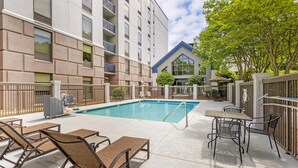 Une piscine entourée de chaises longues et de tables, le tout bordé par un bâtiment doté de balcons et d’un patio couvert.