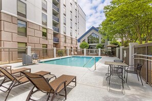 Ein Schwimmbecken mit Liegestühlen und Tischen, umgeben von einem Gebäude mit Balkonen und einer überdachten Terrasse.