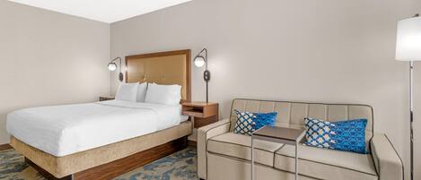 A hotel room with a bed, a sofa, a nightstand, and two wall-mounted lamps.