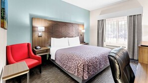A hotel room with a bed, a red armchair, a black leather chair, a nightstand, and a desk.