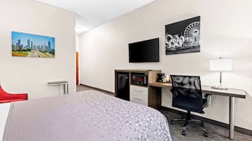 Habitación de hotel con cama, escritorio con computadora, silla, televisor y obras de arte en las paredes.
