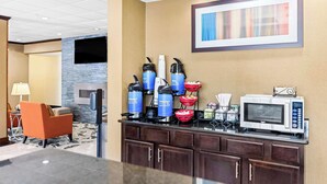 A hotel lobby with a coffee station, seating area, and a framed artwork on the wall.