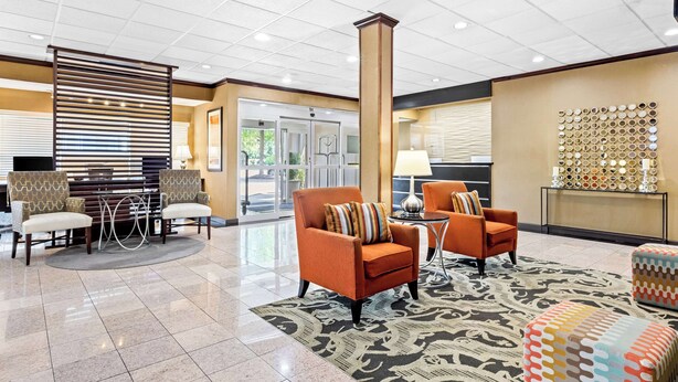 A lobby with two orange armchairs, a patterned rug, and a decorative wall with circular mirrors.