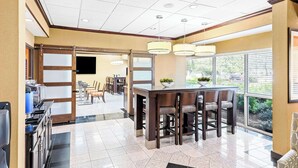 A modern kitchen with a central island, a dining area with chairs, and a large window providing a view of the outdoors.