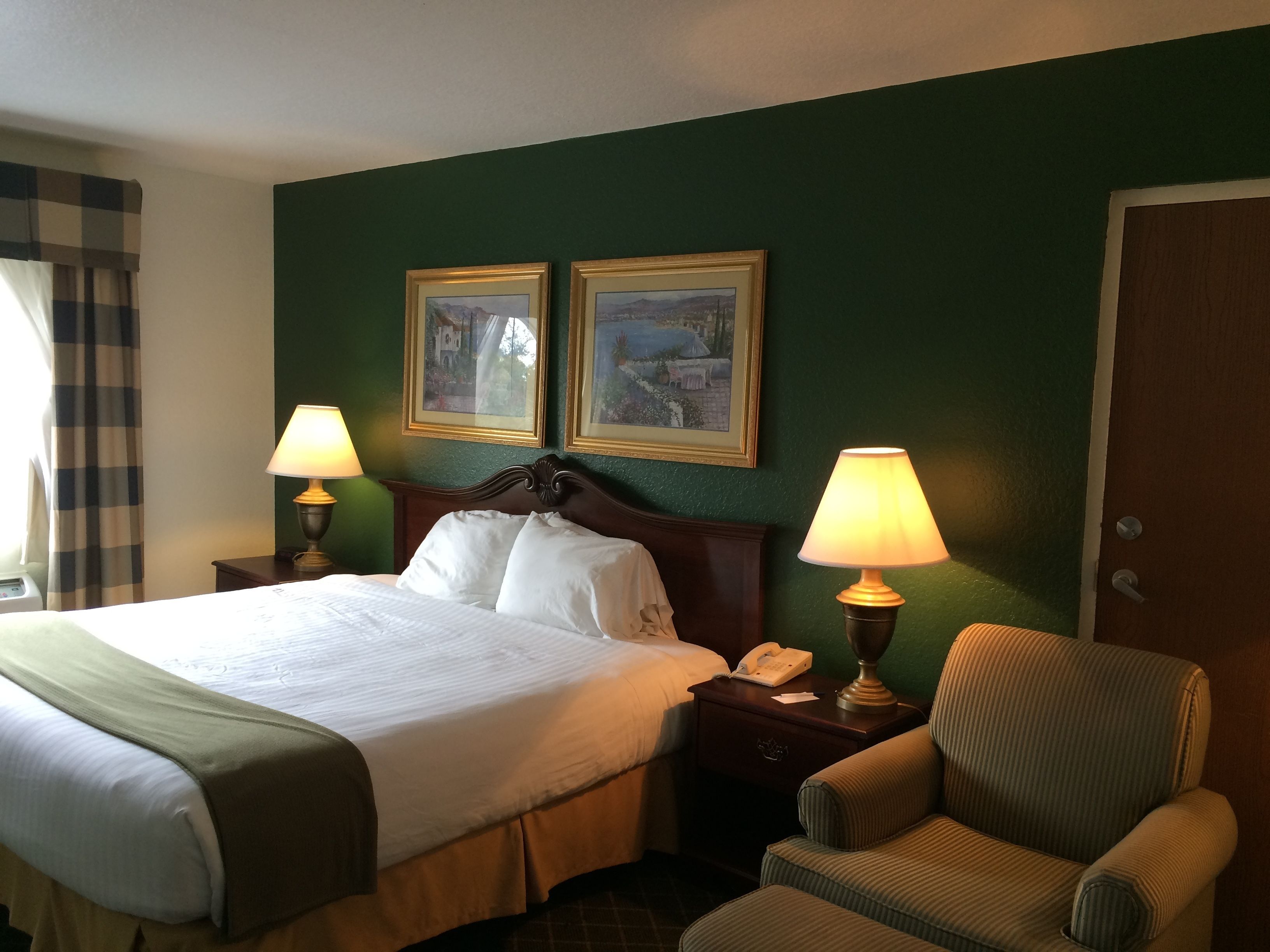 Une chambre d’hôtel avec un grand lit, deux lampes de chevet, une chaise, une table de chevet et deux tableaux encadrés au mur.
