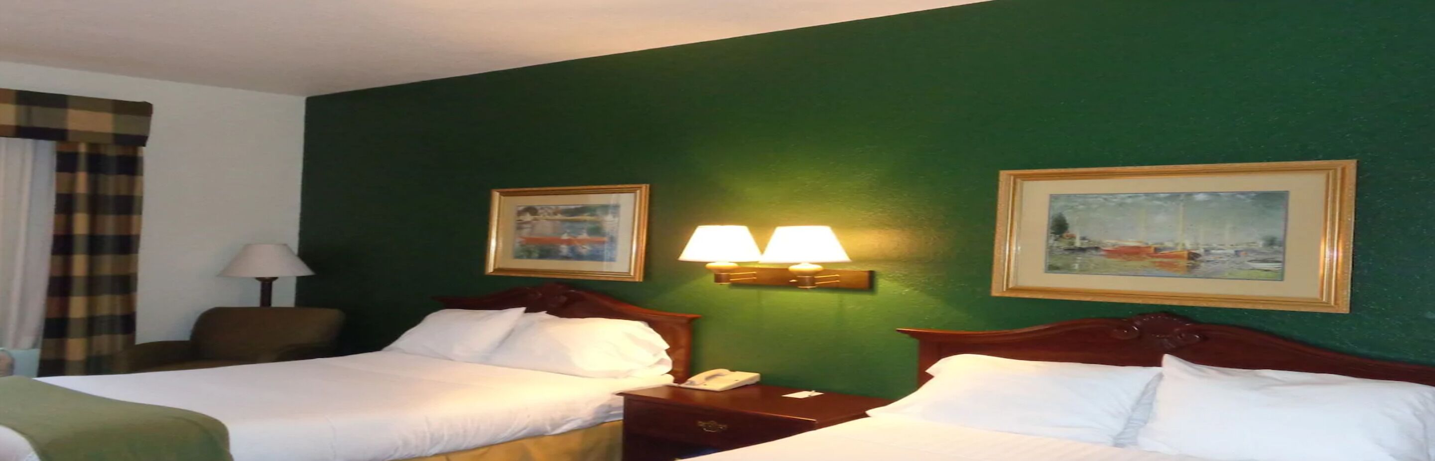 Camera d'albergo con due letti, una parete verde e due quadri appesi.