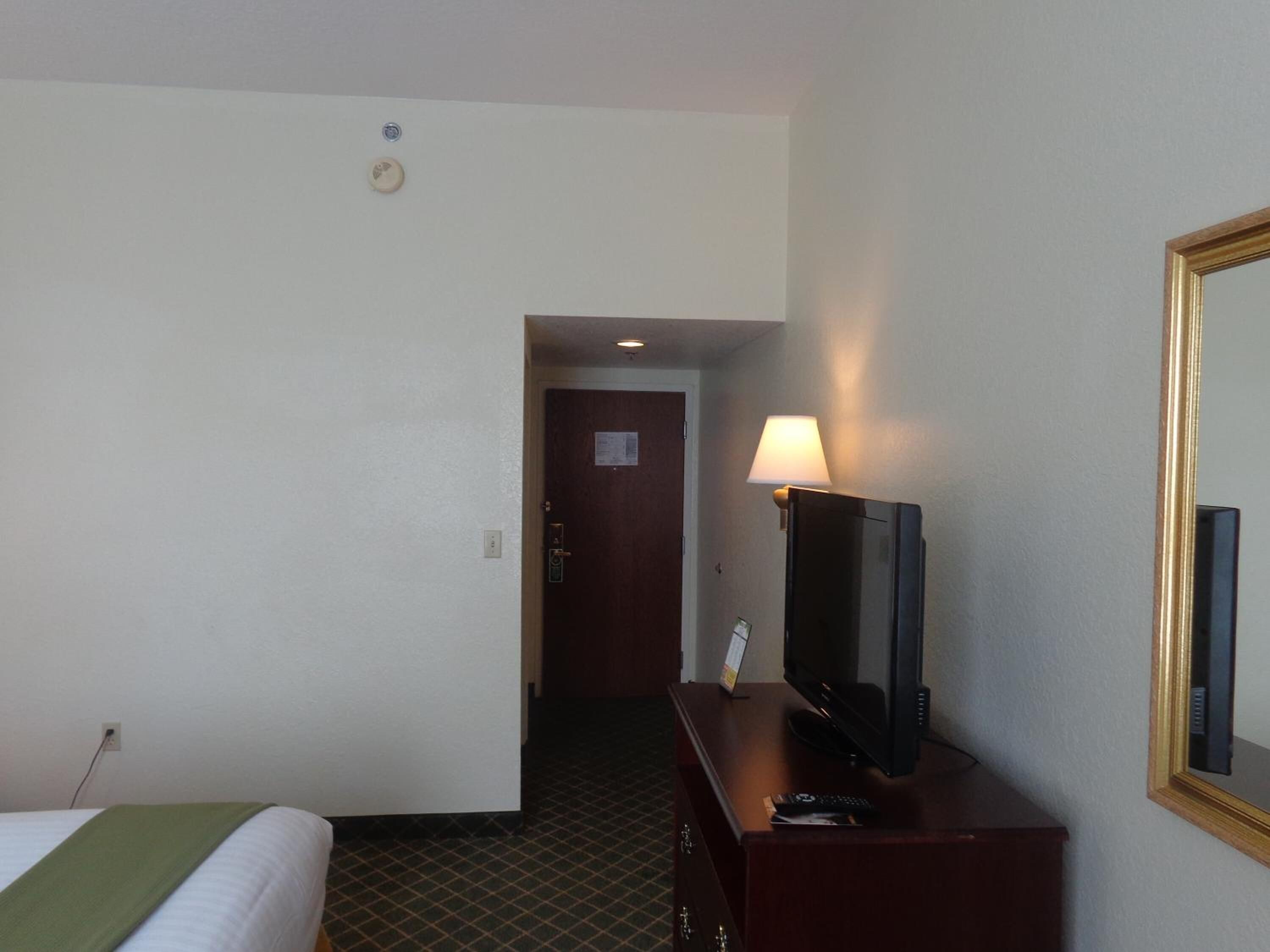 A hotel room with a bed, a desk with a television, a lamp, and a mirror.