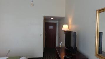 A hotel room with a bed, a desk with a television, a lamp, and a mirror.