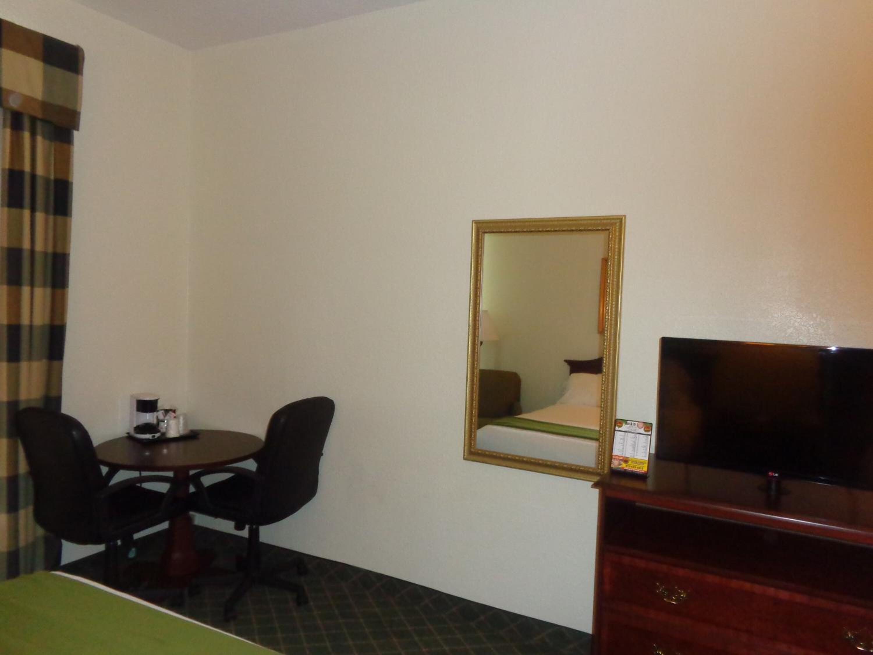 Une chambre d’hôtel comprenant un lit, une télévision, un bureau avec deux chaises, une machine à café et un miroir.