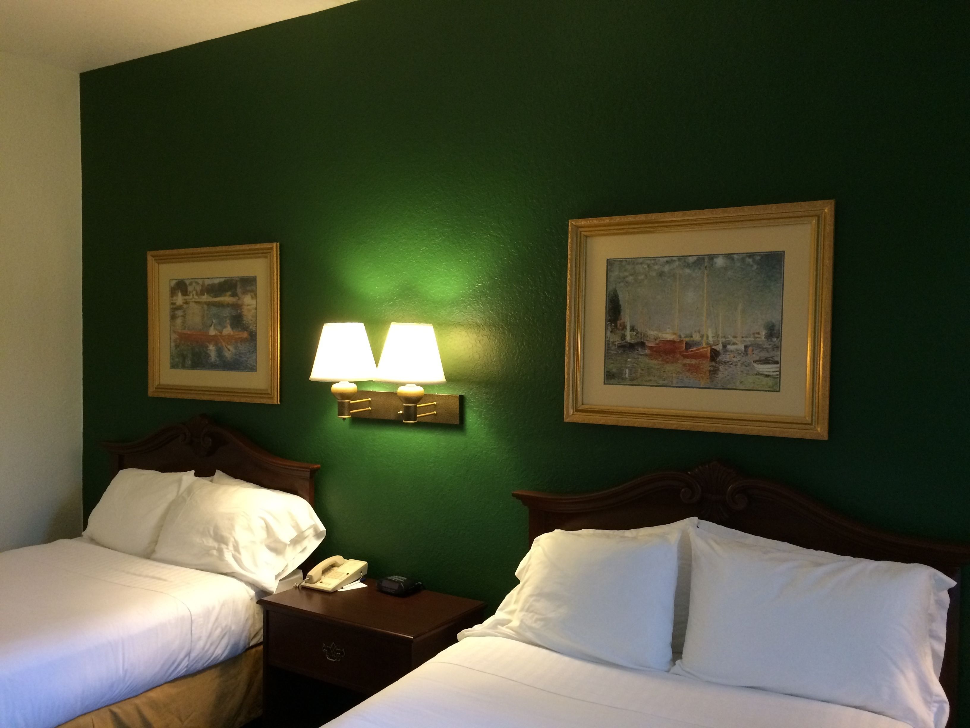 A hotel room with two beds, a nightstand with a phone and a remote, two wall-mounted lamps, and two framed pictures on the wall.