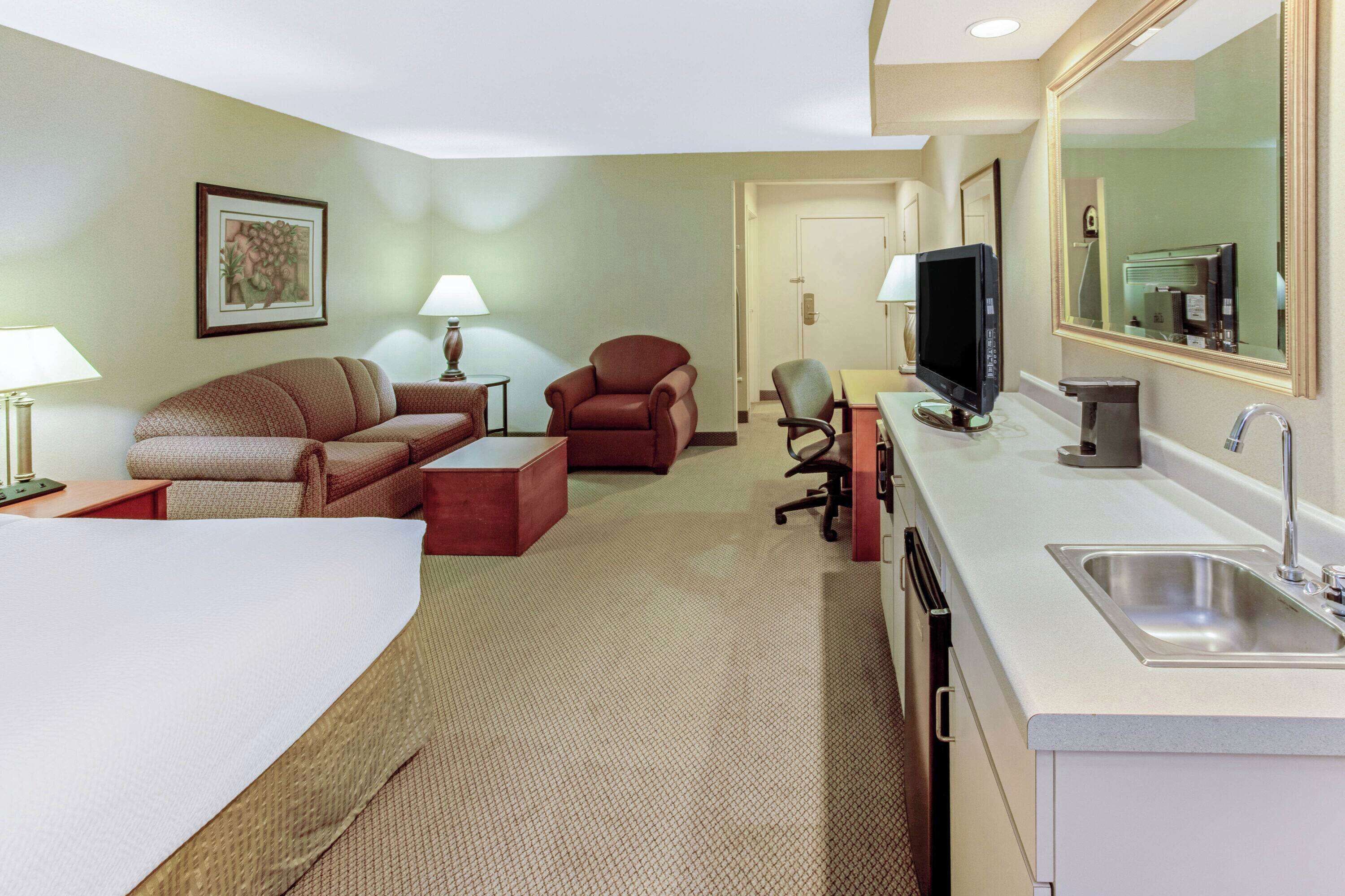 Une chambre d’hôtel comprenant un lit, un canapé, une chaise, un bureau, une télévision et une salle de bain avec un lavabo et un miroir.