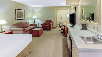 Une chambre d’hôtel comprenant un lit, un canapé, une chaise, un bureau, une télévision et une salle de bain avec un lavabo et un miroir.