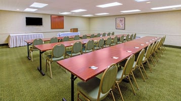 A conference room with multiple tables and chairs, a flat-screen TV, and a carpeted floor.