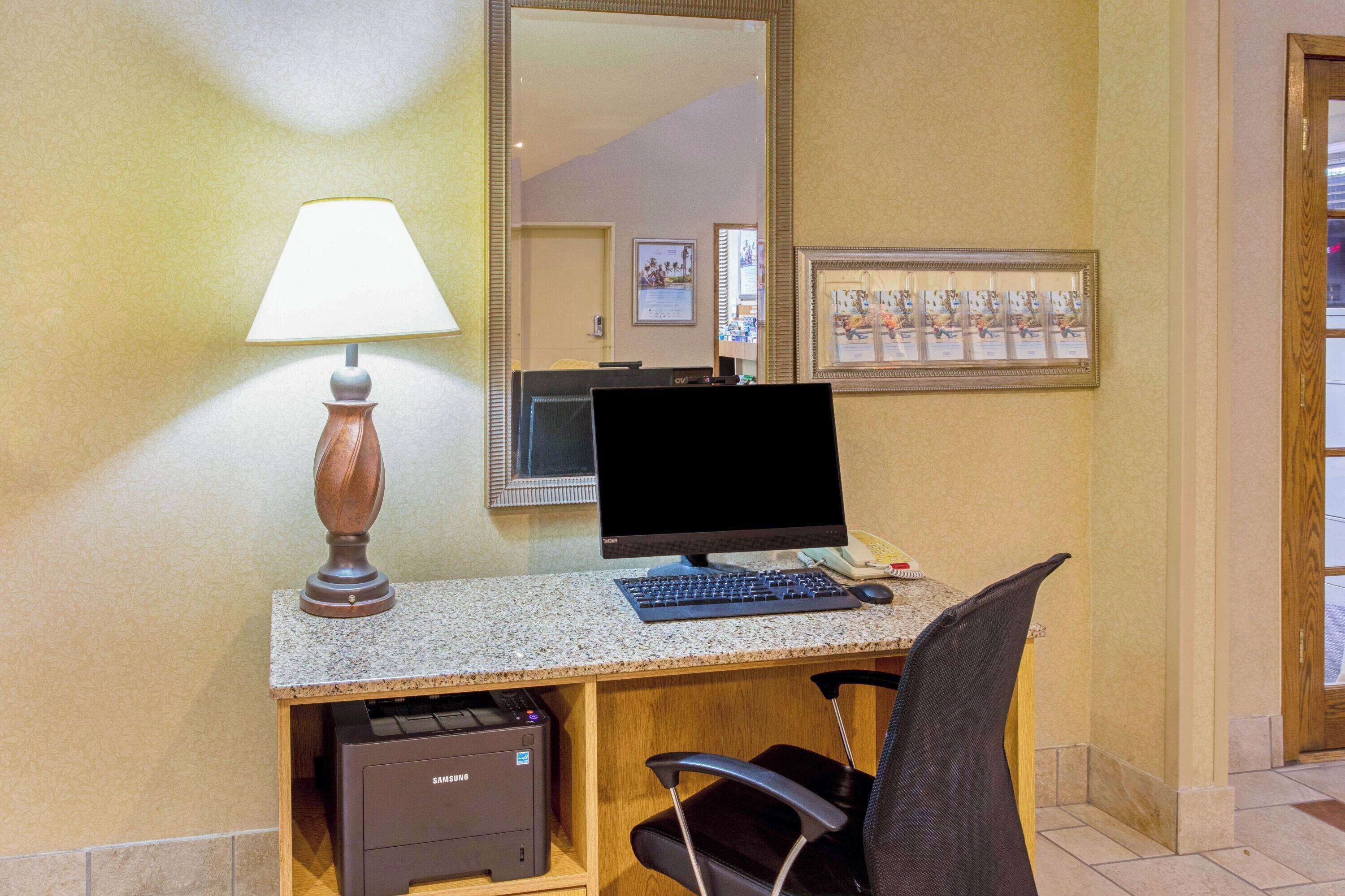 Scrivania in camera d'albergo con computer, lampada, sedia e stampante.