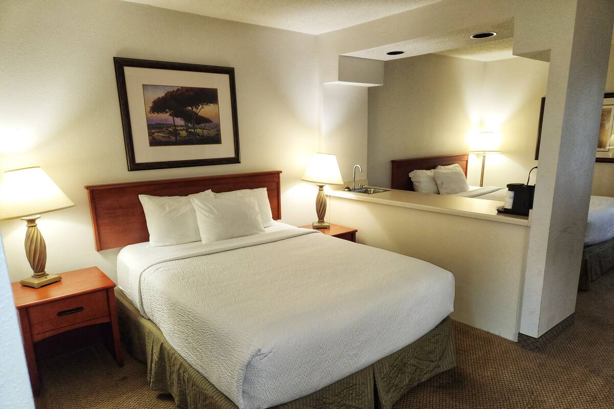 A hotel room with a large bed, two bedside tables with lamps, a nightstand, a mirror, and a framed picture on the wall.
