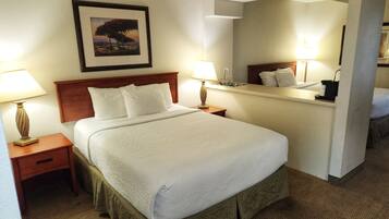 A hotel room with a large bed, two bedside tables with lamps, a nightstand, a mirror, and a framed picture on the wall.