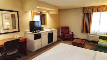 A hotel room with a bed, desk, chair, kitchenette, and a window with curtains.