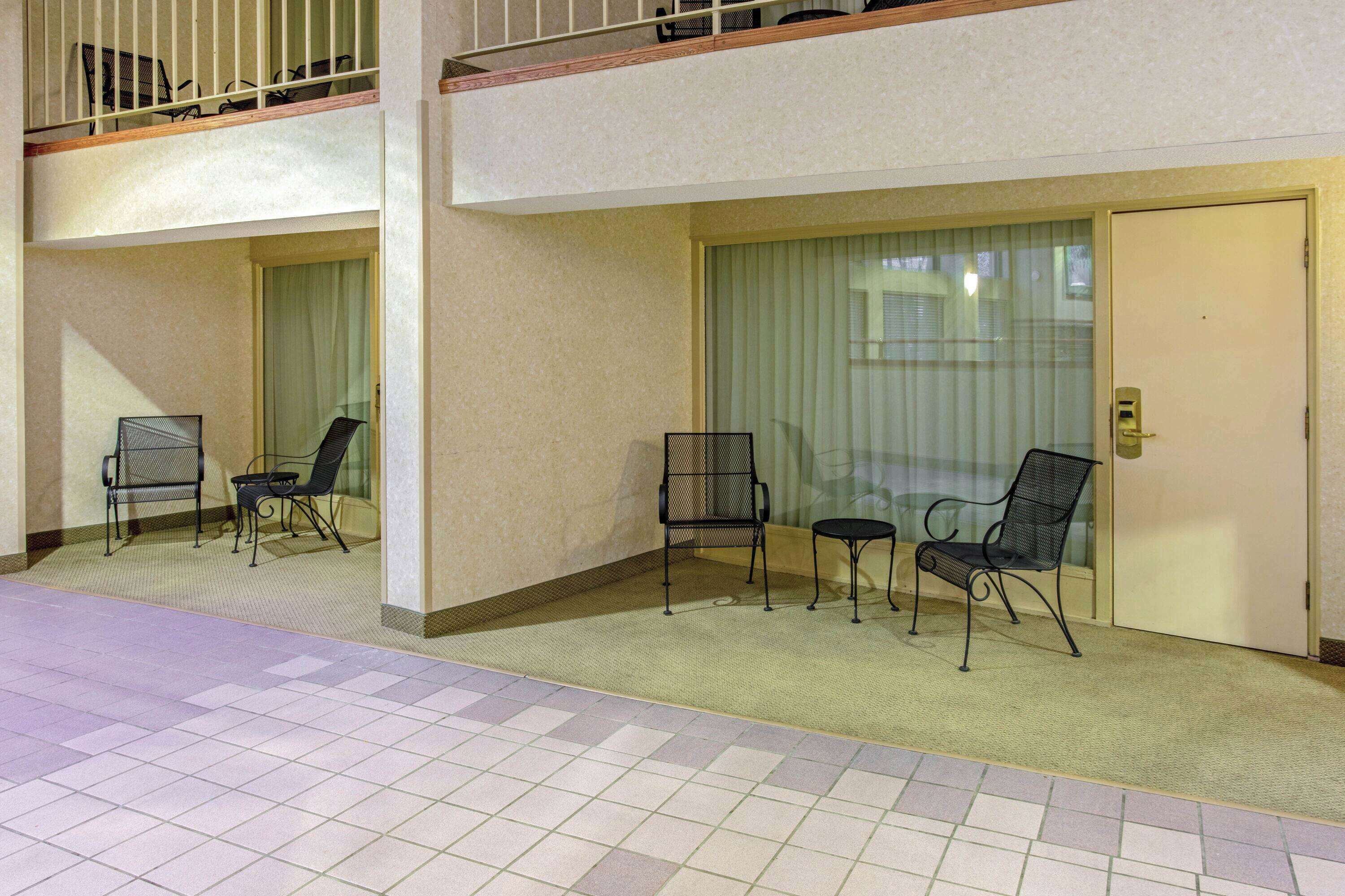 A hotel corridor with a balcony, a door with a keypad lock, and a seating area with chairs and a small table.