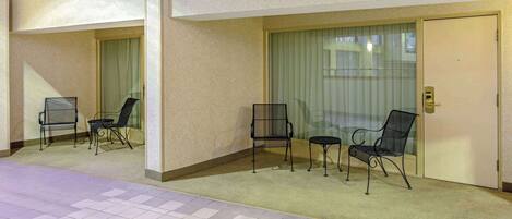 A hotel corridor with a balcony, a door with a keypad lock, and a seating area with chairs and a small table.