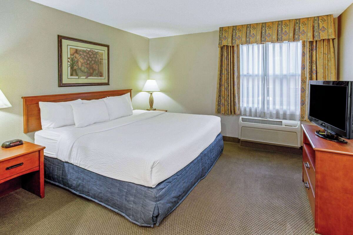 A hotel room with a bed, a TV, a desk with a lamp, and a picture on the wall.