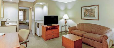 A hotel room with a sofa, a TV, a desk, and a lamp.