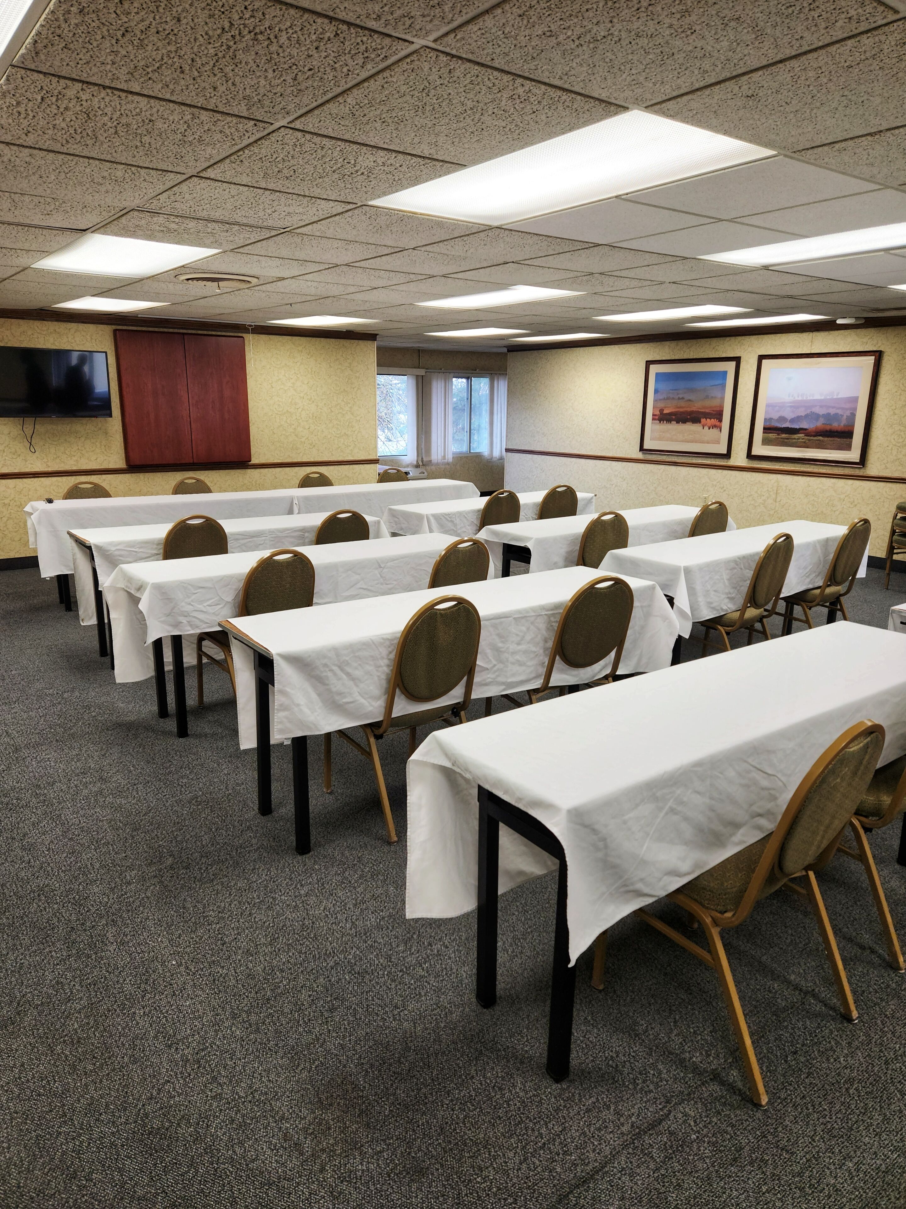 A conference room with multiple tables and chairs, a flat-screen TV on the wall, and framed pictures on the wall.