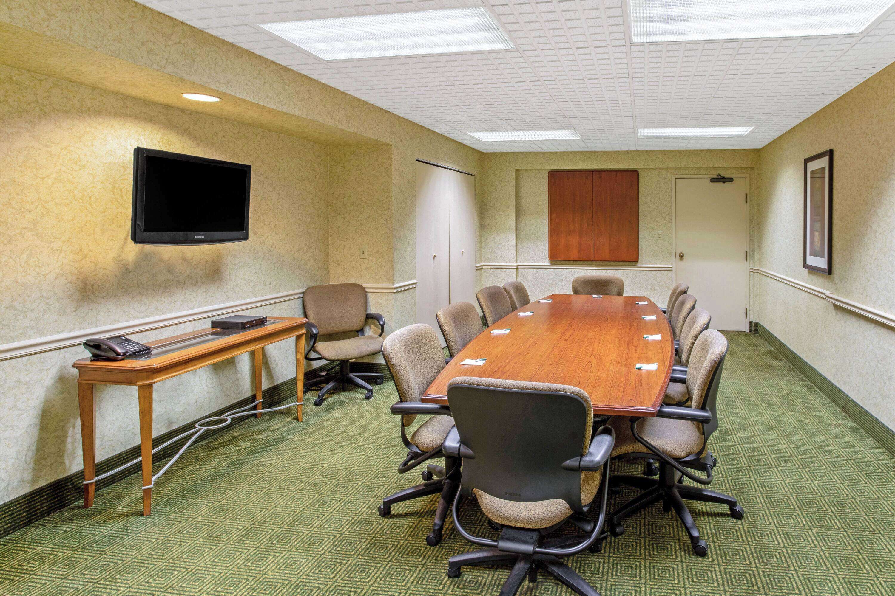 A conference room with a long table, chairs, a TV mounted on the wall, and a door with a wooden panel.