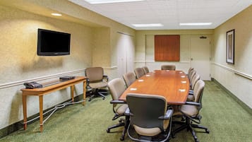 Una sala de conferencias con una larga mesa, sillas, un televisor montado en la pared y una puerta con panel de madera.