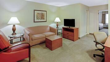 A hotel room with a striped sofa, a red armchair, a wooden coffee table, a television on a wooden stand, and a lamp on a side table.