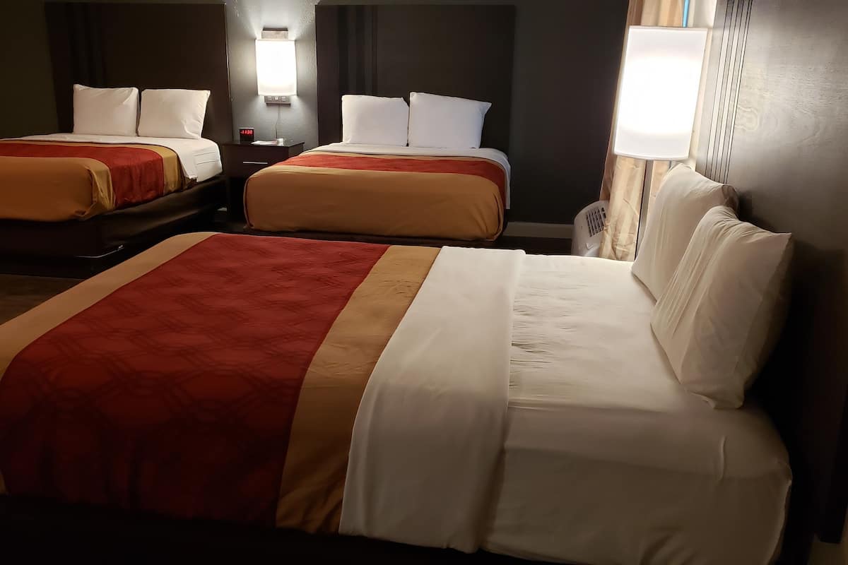 A hotel room with two beds, each with a red and white bedspread, and a nightstand with a lamp between them.