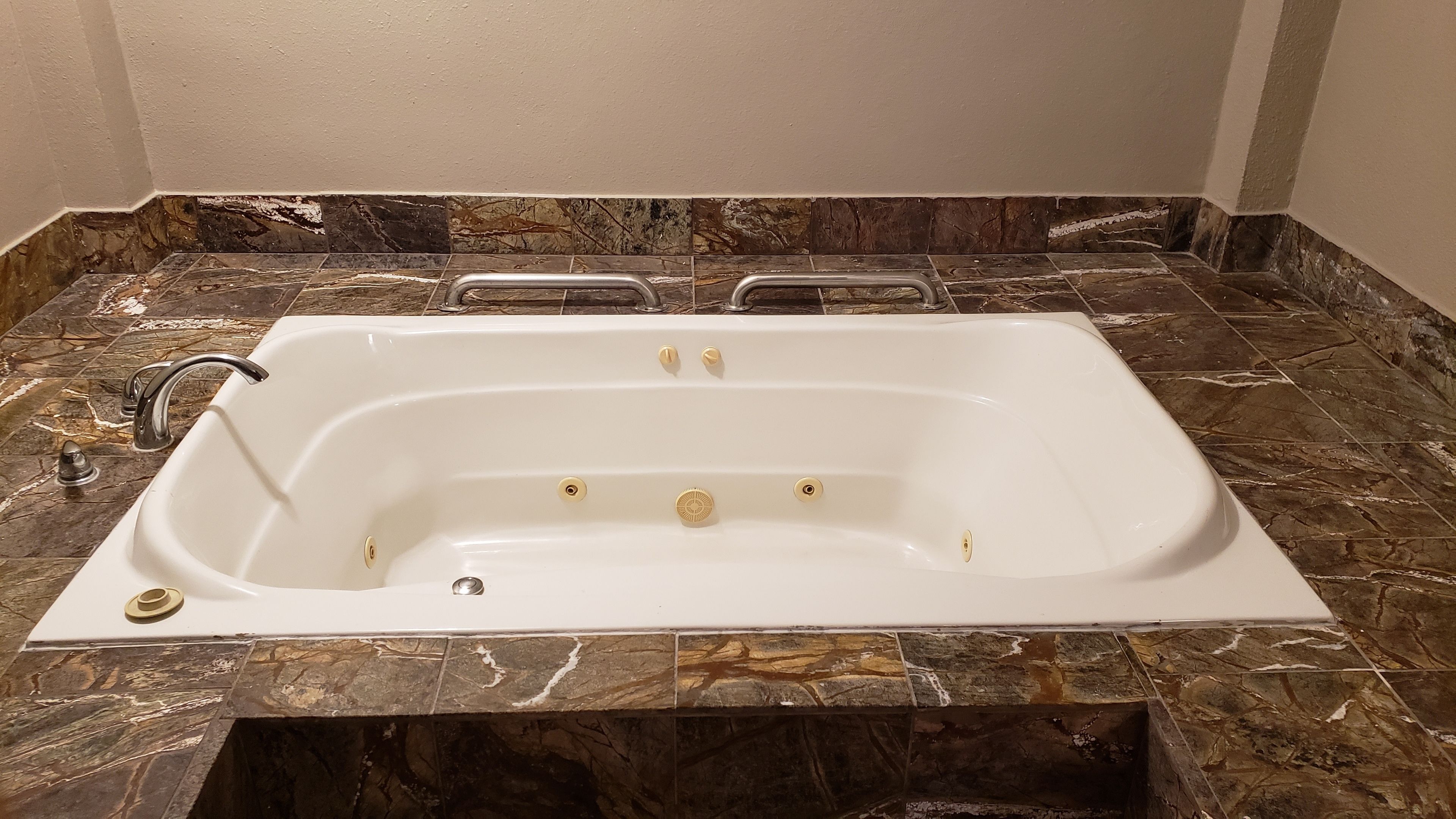 Une baignoire rectangulaire, dotée de deux robinets et d’une molette de réglage, posée sur un sol carrelé en marbre.