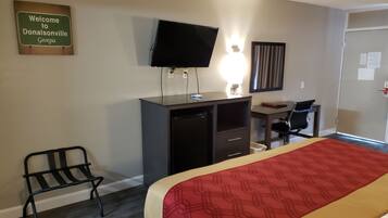 Una habitación de hotel con cama, escritorio, silla, televisor y un cartel en la pared.
