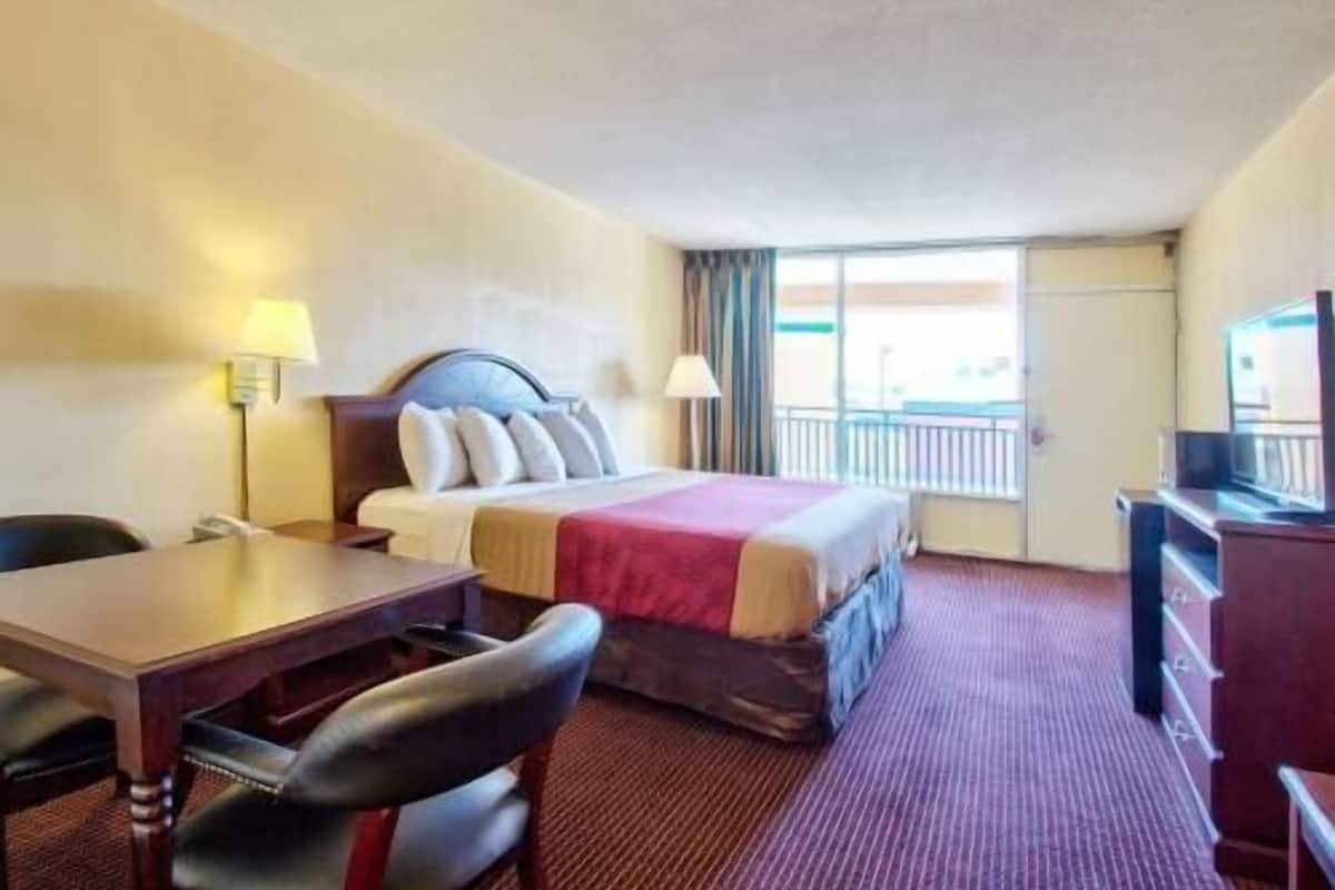 A hotel room with a bed, a desk, a chair, a dresser, and a window with a view.
