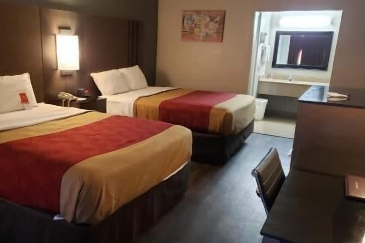 A hotel room with two beds, a desk, a chair, a lamp, and a window.