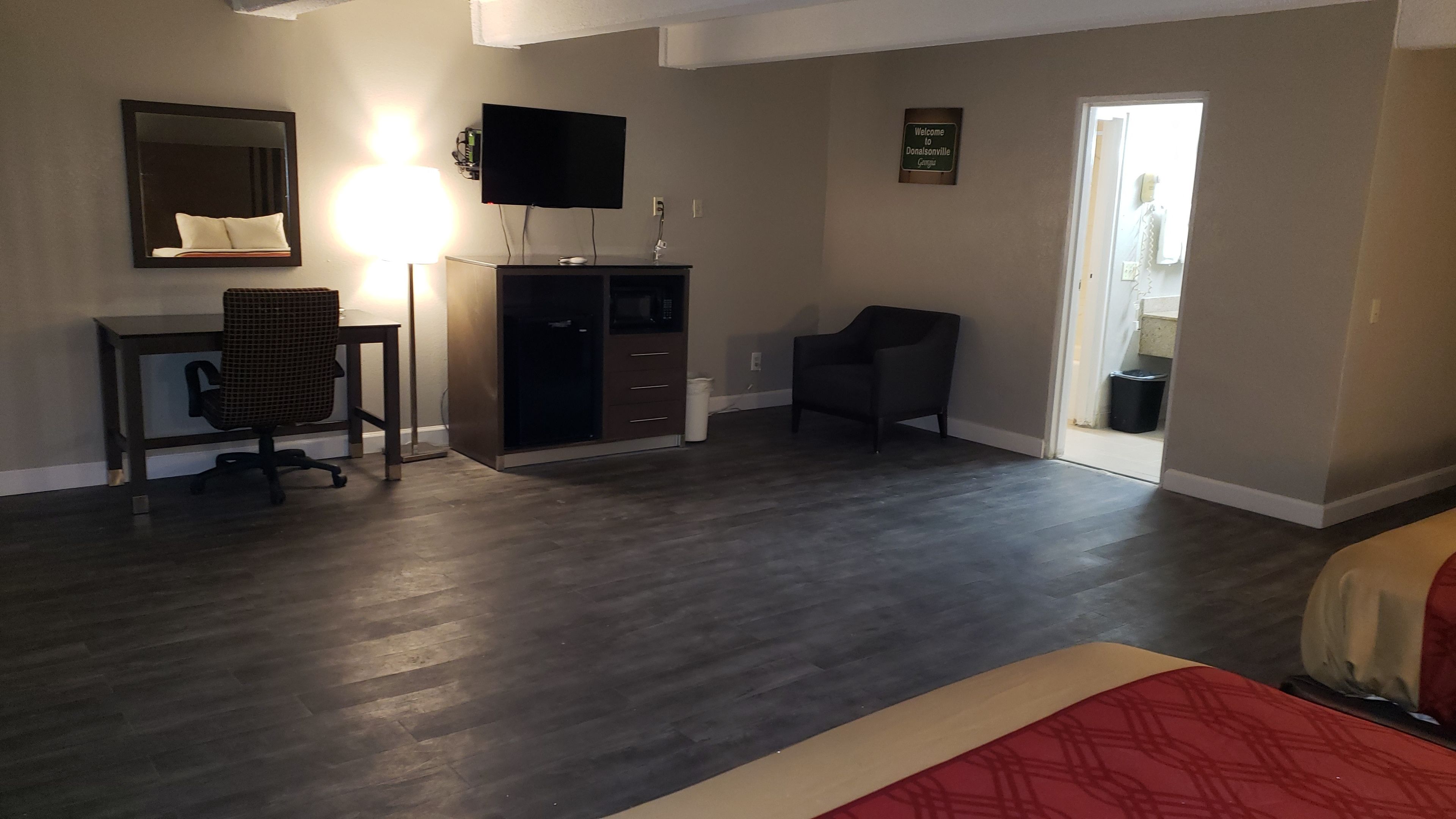 A hotel room with a desk, chair, TV, wardrobe, and a view of the outside.