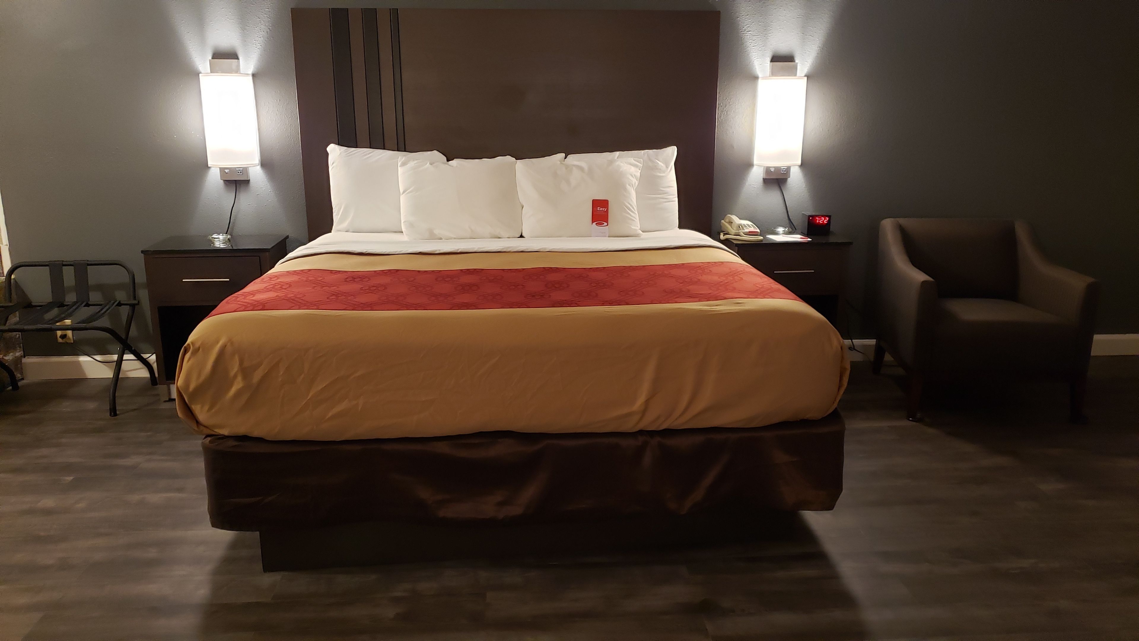 Una habitación de hotel con una cama, dos mesitas de noche, una silla y un aparador.