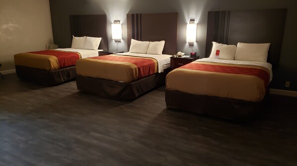 A hotel room with three beds, each with a red and beige bedspread, white pillows, and a nightstand with a clock. - Econo Lodge Donalsonville (Donalsonville)