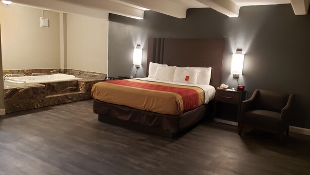 Una habitación de hotel moderna con una cama grande, una bañera integrada y una zona de estar separada.