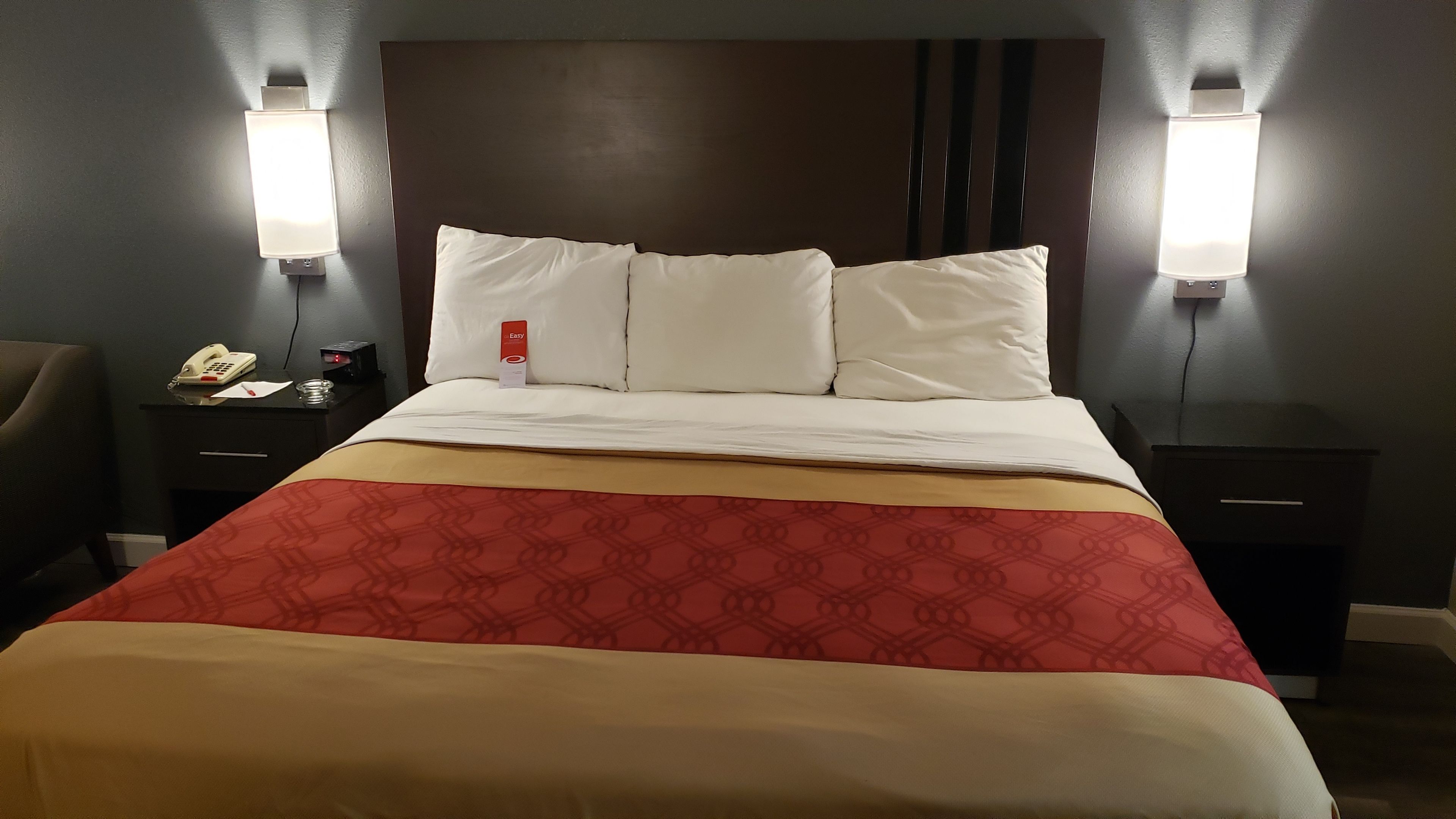 Ein Hotelzimmer mit einem großen Bett, zwei Nachttischen, einem Beistelltisch, einem Telefon und einem Schild, das die Zimmerverfügbarkeit anzeigt.