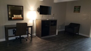 Habitación de hotel con televisión de pantalla plana montada en la pared, un escritorio con silla, microondas y un mueble pequeño.