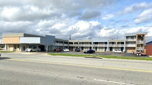 Un motel de varios pisos, con estacionamiento y varios coches aparcados al frente.