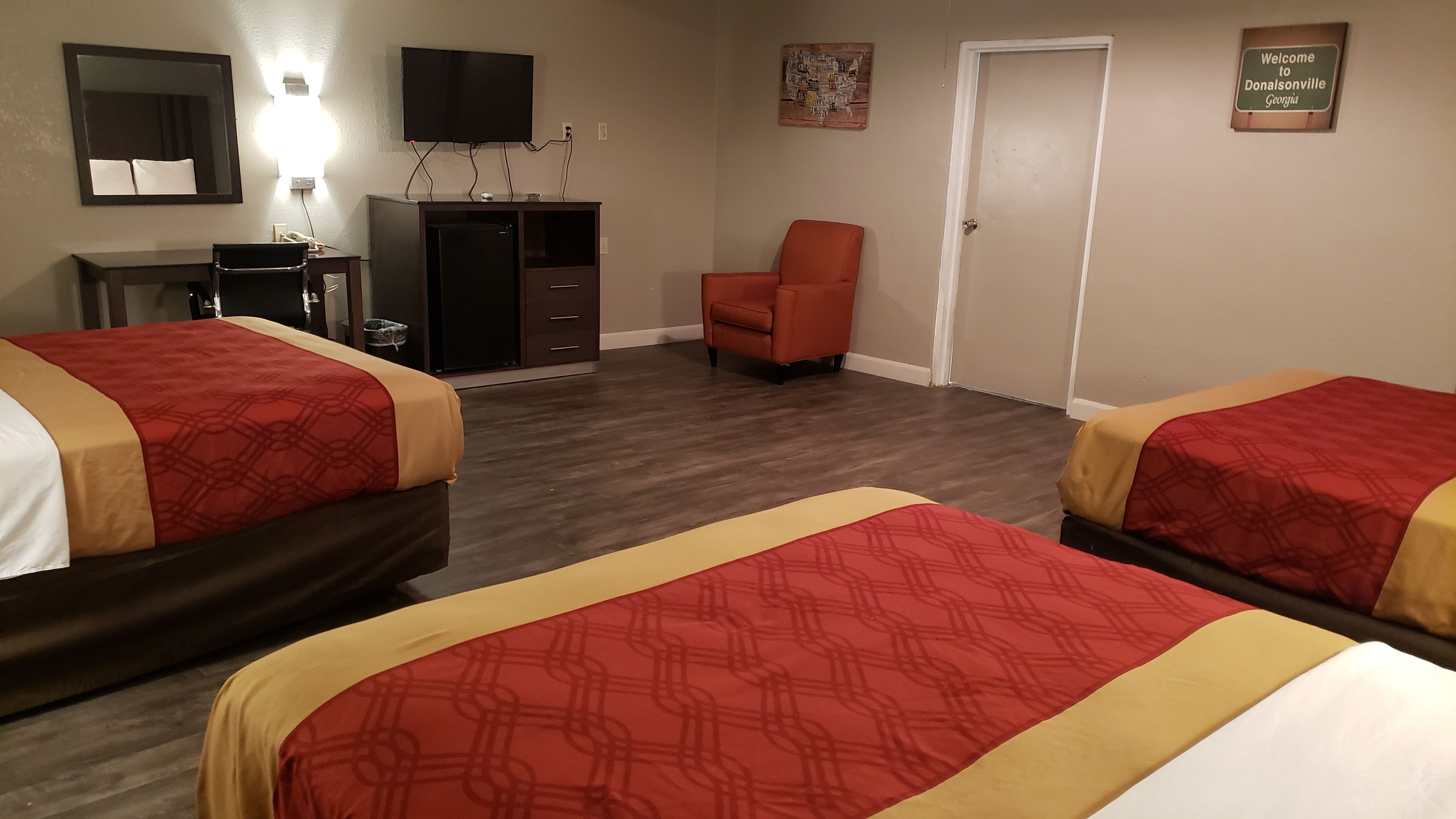 A hotel room with two beds, a desk with a computer, a TV, and a door with a welcome sign.