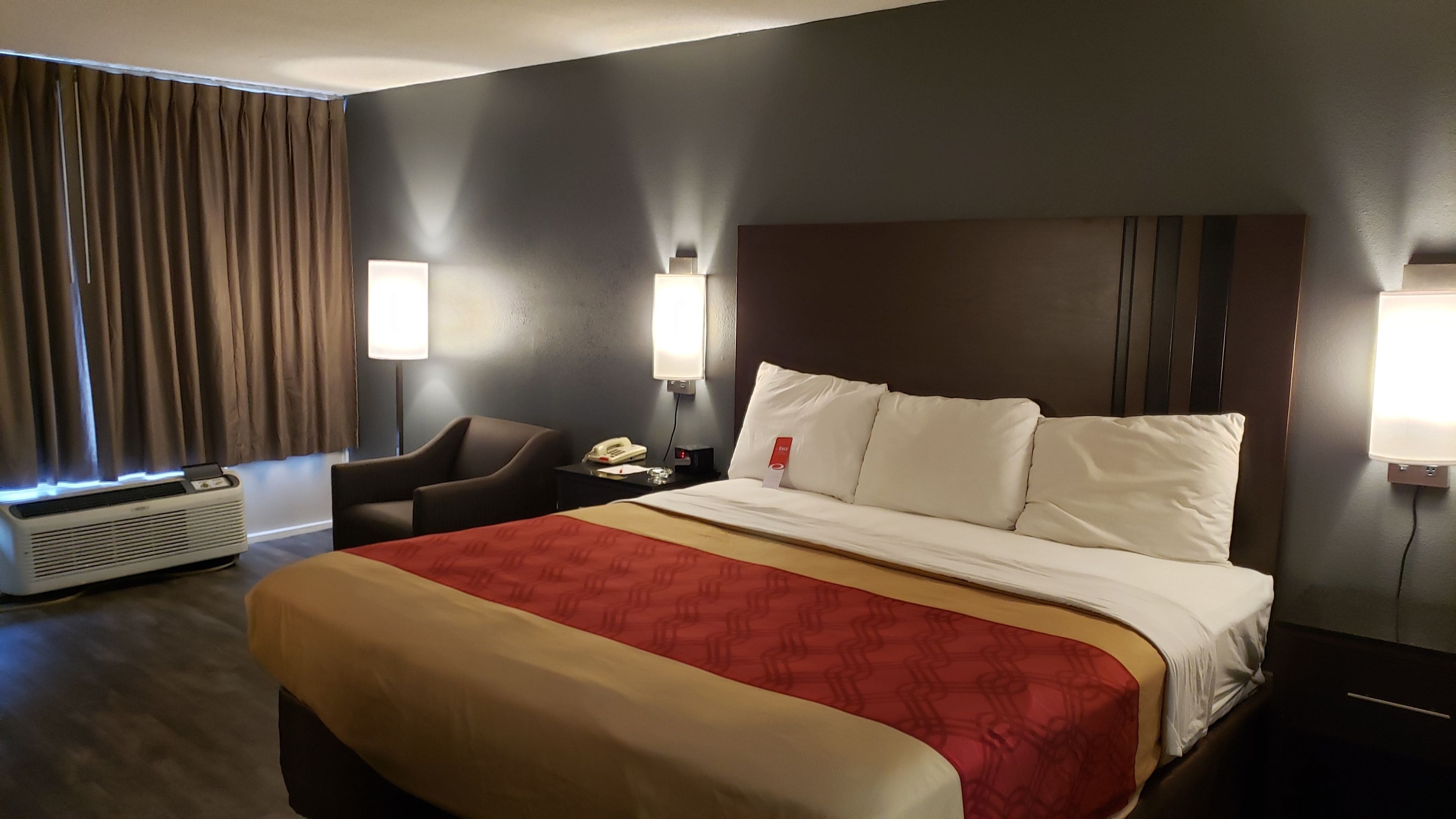 Una habitación de hotel con una cama grande, una silla, un escritorio con teléfono y una lámpara de pared.