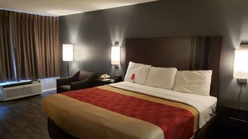Una habitación de hotel con una cama grande, una silla, un escritorio con teléfono y una lámpara de pared.