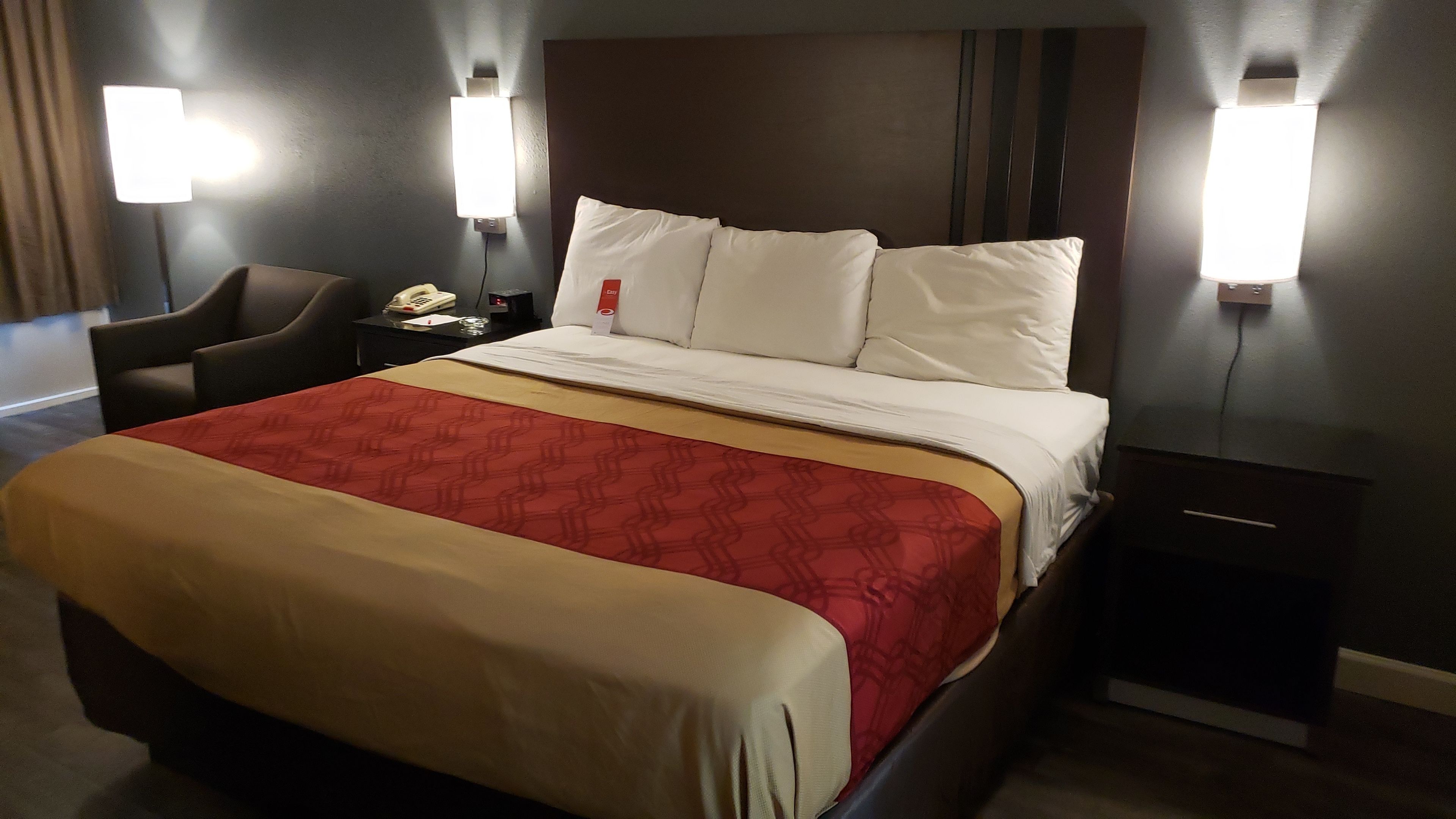 Une chambre d’hôtel comprenant un lit, une table de chevet, une chaise et deux lampes fixées au mur.
