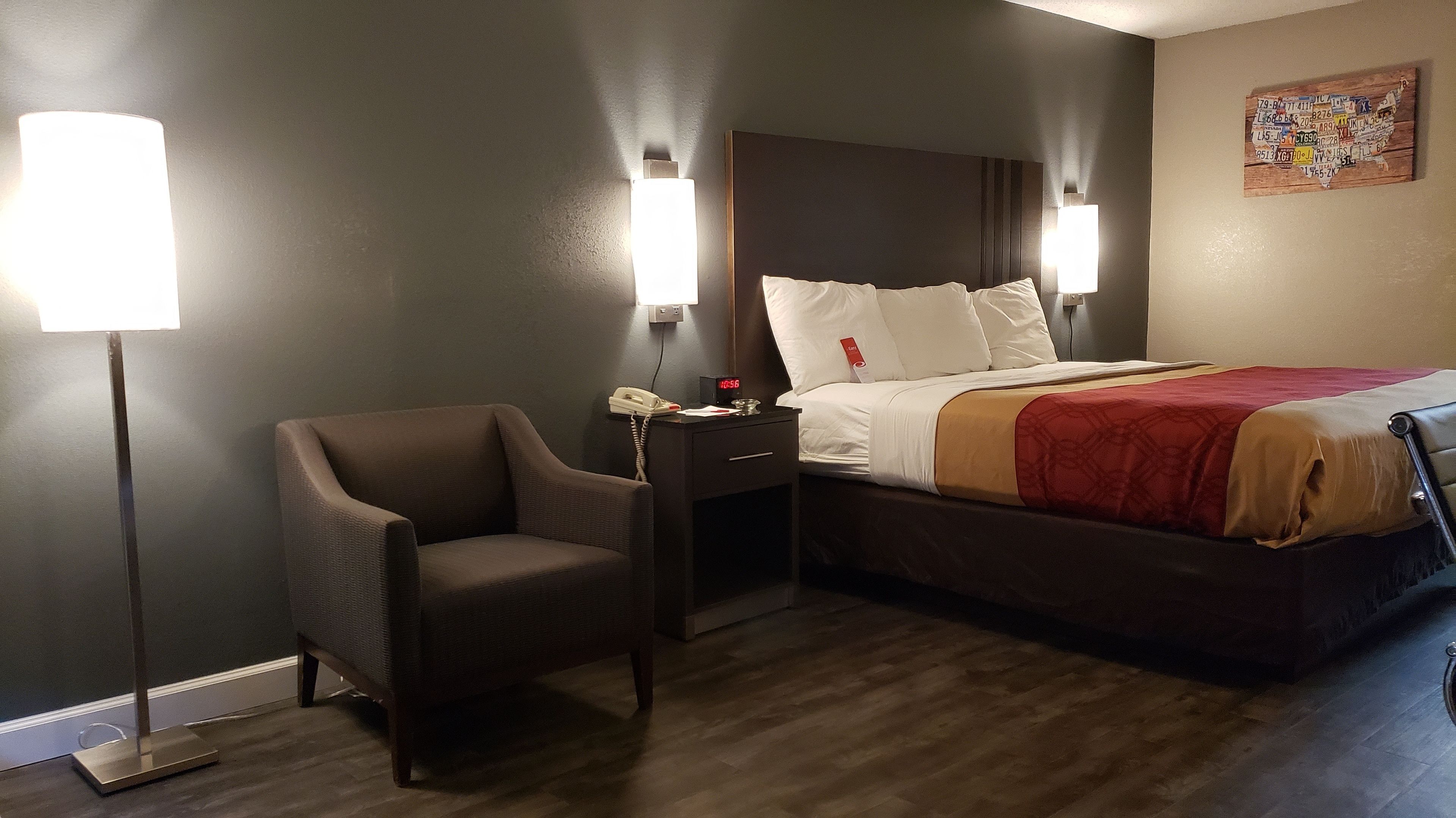 A hotel room with a bed, a chair, a nightstand with a phone, and wall-mounted lights.