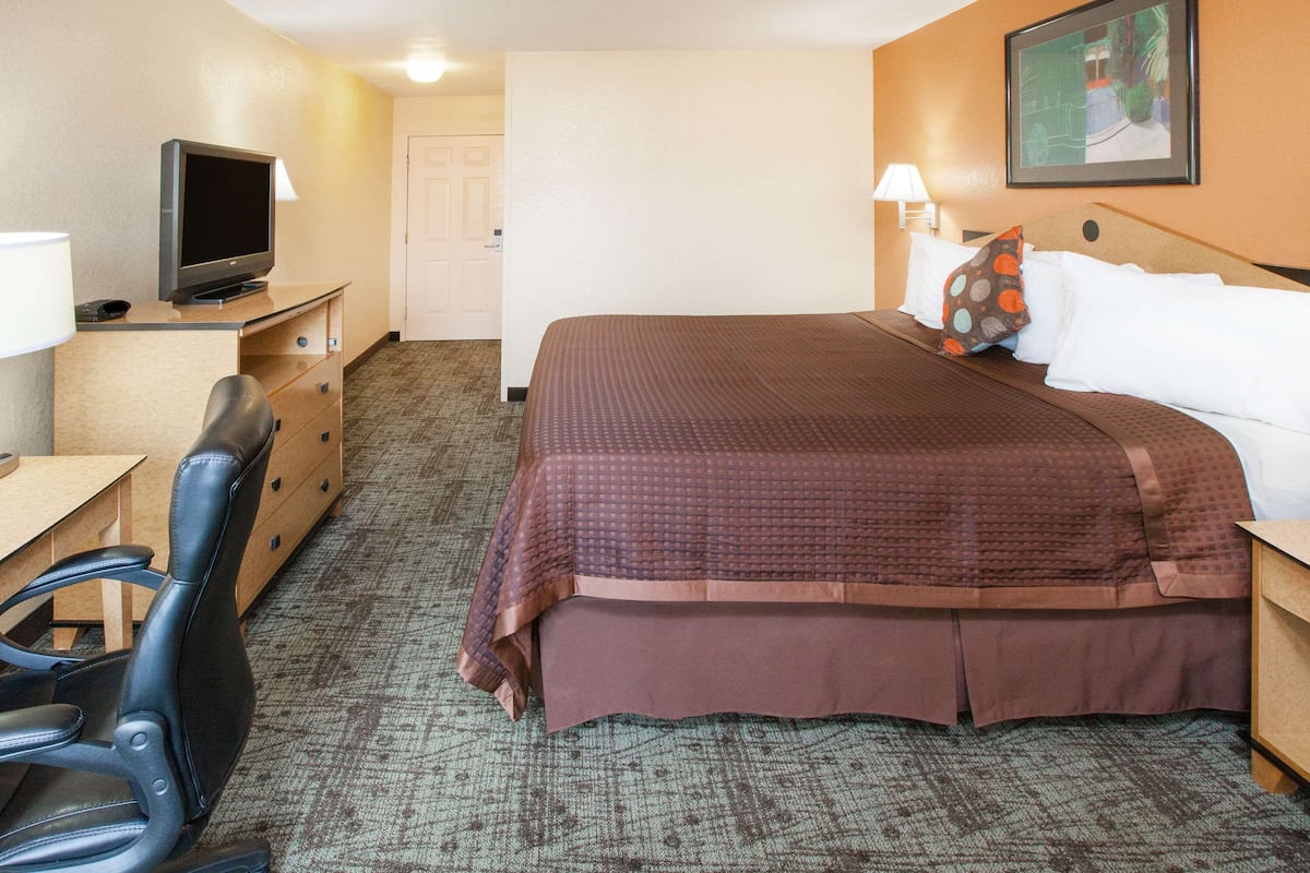A hotel room with a bed, a desk with a television, a chair, and a door.