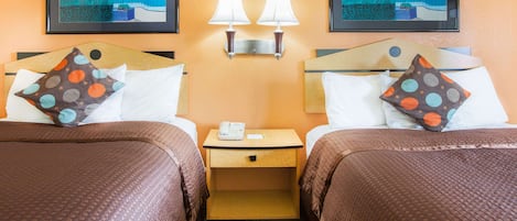 Habitación de hotel con dos camas, cada una con una almohada, una mesita de noche con un teléfono y dos lámparas fijadas a la pared.